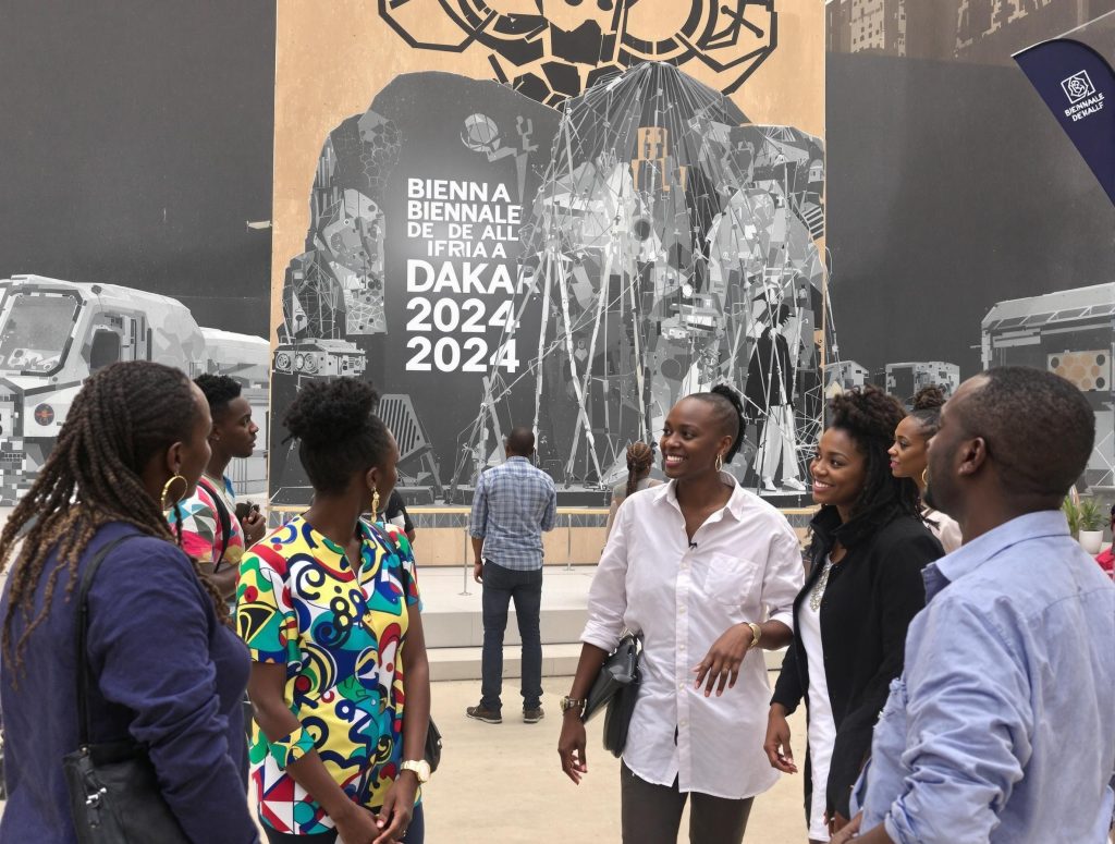 groupe d'artistes africains à la biennale de dakar 2024 au sénégal devant une installation monumentale